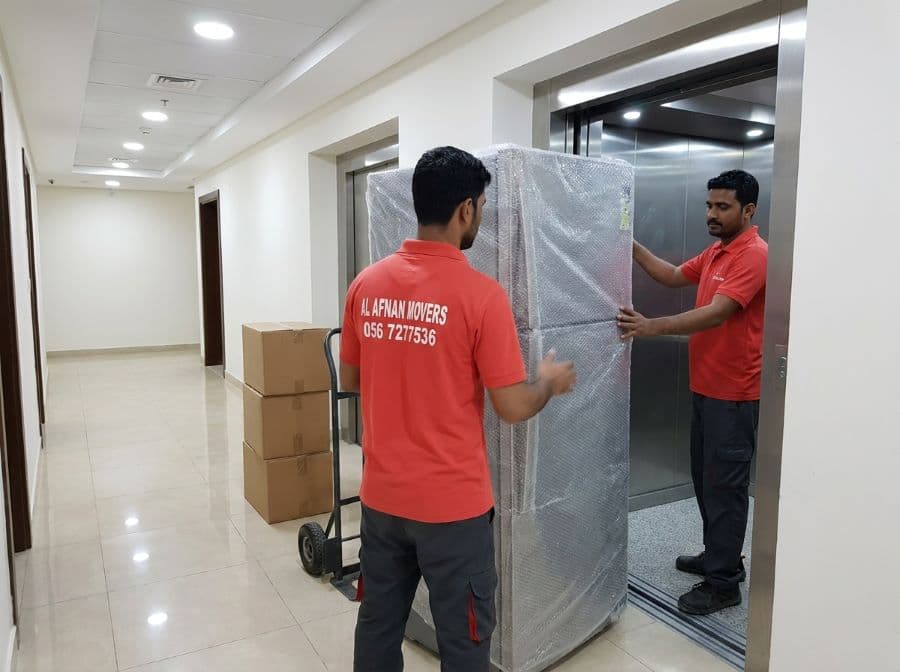 Al Afnan apartment movers carrying wrapped furniture into a building service lift