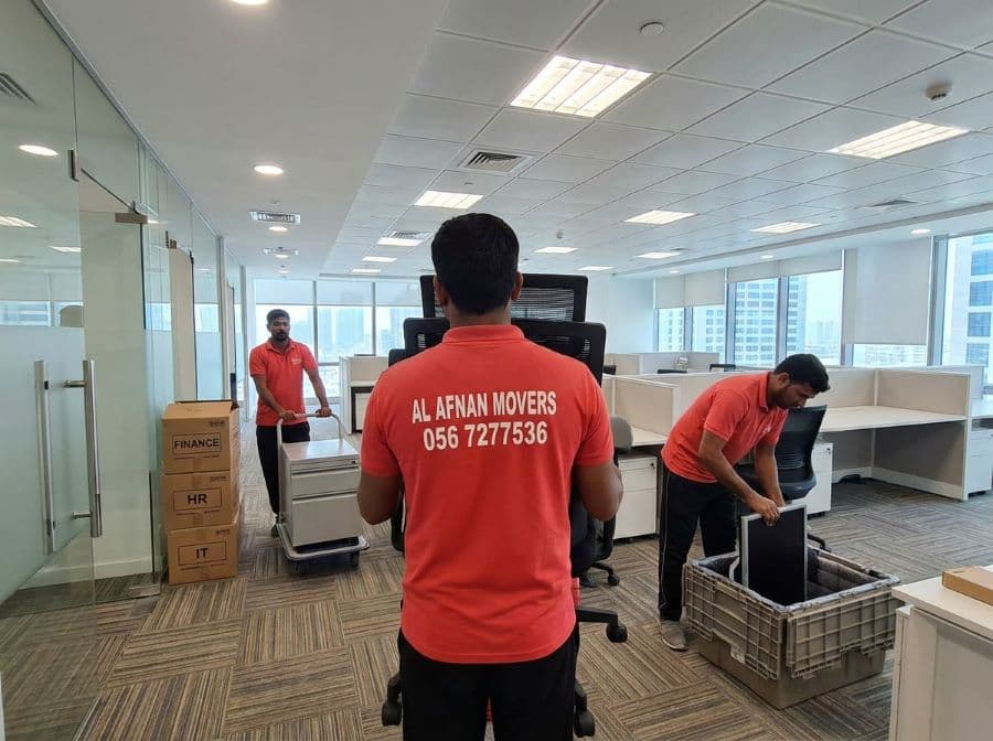 Al Afnan office movers wheeling filing boxes and a wrapped office chair out of an office